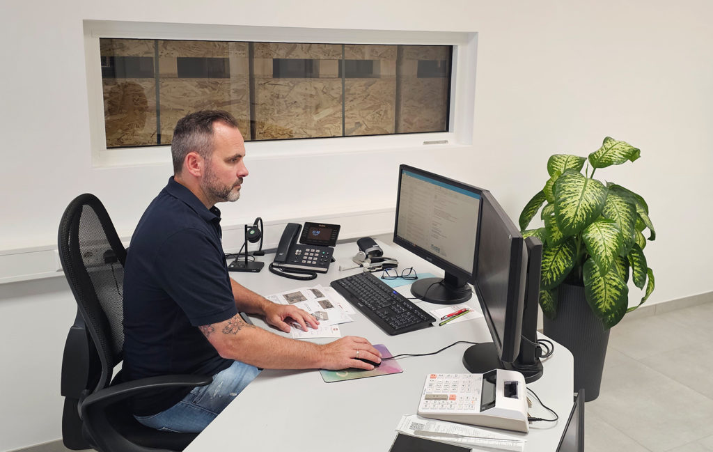 Herr Weber am Schreibtisch beim Konstruieren von Industrieverpackungen (im Hintergrund grüne Pflanze)